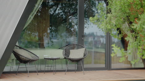 Outdoor-patio-with-two-modern-black-chairs-and-a-small-table,-adjacent-to-large-glass-doors-and-surrounded-by-greenery