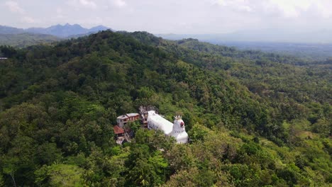 Aerial-view-of-The-white-chicken-shaped-church-building-was-built-in-the-middle-of-a-hill-with-lush-trees