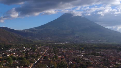 Antigua-Guatemala-Mit-Einem-Markanten-Kreuz-Im-Vordergrund,-Mit-Blick-Auf-Die-Stadtlandschaft-Vor-Der-Kulisse-Eines-Hoch-Aufragenden-Vulkans-Unter-Einem-Wolkigen-Himmel