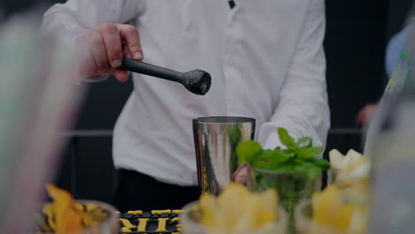 Bartender-preparing-a-cocktail,-using-a-muddler,-with-fresh-ingredients-on-the-counter