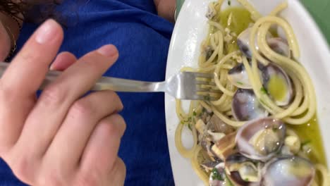 Vertical-video-of-European-woman's-hand-eating-spaghetti-roll-pasta-with-fork