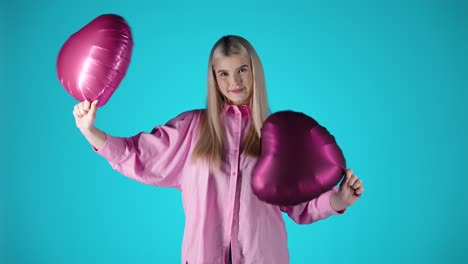 Hübsche-Blonde-Frau-Mit-Wehenden-Lila-Herzballons-Vor-Blauem-Hintergrund,-Farbenfrohe-Studioaufnahme