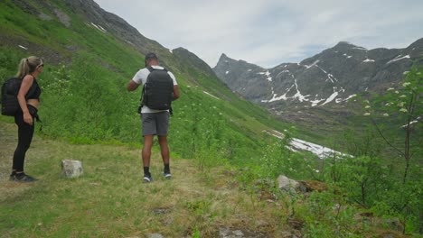 Couple-hiking-in-scenic-Norway-mountains-with-lush-greenery-and-snowy-peaks-in-the-background