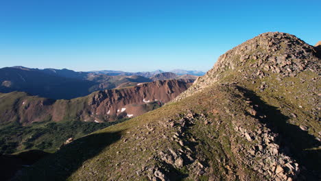 Aerial-View-of-Lonely-Female-Hiker-Walking-on-Hill-With-Stunning-View-of-Mountain-Landscape-on-Sunny-Day