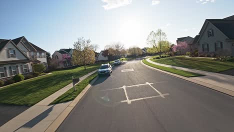 Unique-street-flight-of-a-FPV-drone-in-a-middle-class-town-between-single-family-houses,-towards-the-sun-on-a-warm-spring-day