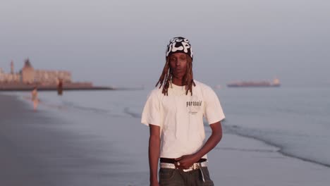 an-African-man-male-man-model-boy-walks-and-poses-on-the-beach-seashore-ocean-water-in-the-sunset