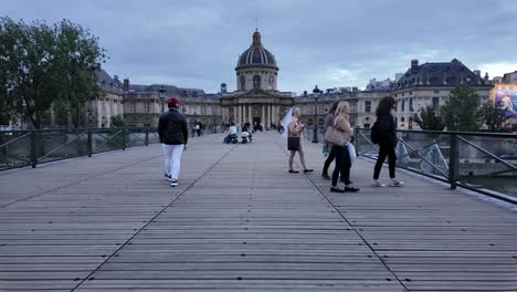 Tourists-visiting-Pont-des-Arts-with-Institut-de-France-on-background-in-Paris