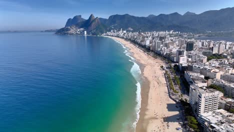 Experience-a-breathtaking-4K-drone-flyover-of-Ipanema-Beach,-showcasing-Rio-de-Janeiro's-skyline,-white-sandy-shores,-and-scenic-mountains-in-the-background