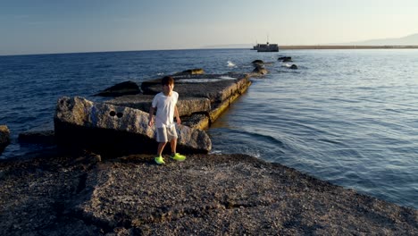 Medium-shot-of-8-years-old-caucasian-boy,-walking-towards-the-sun-on-a-pier-at-sea-Kalamata,-enjoying-his-summer-vacations-4K