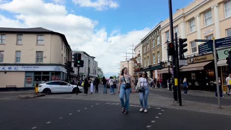 Greenwich,-London:-Crossing-a-street-in-the-city-center-of-Greenwich,-surrounded-by-bustling-shops,-restaurants,-and-vibrant-daily-activity