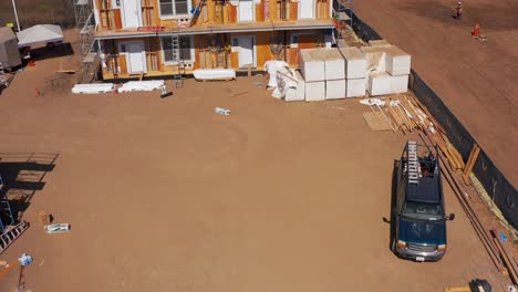 Aerial-low-tilting-up-shot-of-construction-crew-working-on-the-siding-of-a-pre-fab-unit-at-a-modular-housing-development-site-in-West-Los-Angeles,-California