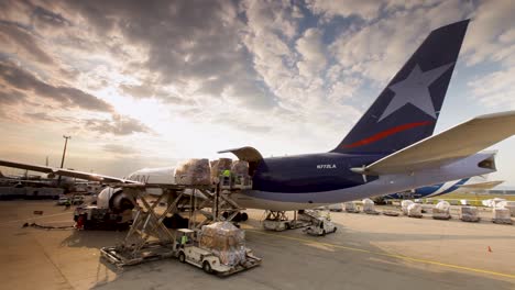 Sunset-at-an-airport-as-cargo-is-loaded-onto-a-commercial-airliner,-vibrant-sky-in-the-background