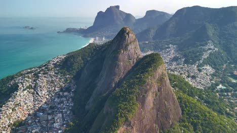 Drone-footage-of-Rio-de-Janeiro-on-a-bright-sunny-day,-showcasing-Dois-Irmaos-Mountain,-the-vibrant-favelas,-surrounded-by-lush-forests,-and-stunning-beaches-from-a-breathtaking-aerial-perspective