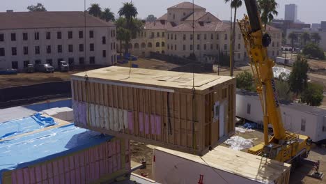 Aerial-close-up-panning-shot-of-a-heavy-duty-crane-moving-a-pre-fab-housing-module-into-position-at-a-construction-site-in-West-Los-Angeles,-California