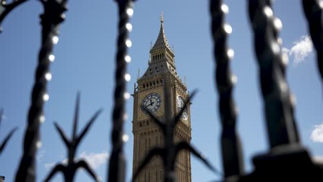 Big-Ben-behind-beautifully-twisted,-sharp-ornate-iron-fence-bars-against-a-clear-blue-sky,-symbolizing-separation-and-grandeur-amidst-modern-urban-civilization