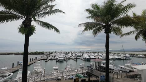 Docked-boats-at-the-Marina-Pez-Vela-with-the-Pacific-Ocean-and-surrounding-coastline-in-the-background-on-a-windy-day-in-Quepos,-Costa-Rica