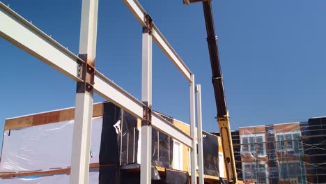 Gimbal-booming-down-shot-of-construction-workers-operating-a-cherry-picker-lift-crane-at-a-modular-housing-site-in-West-Los-Angeles,-California