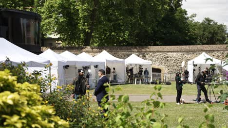 Periodistas-Preparando-Su-Equipo-En-Una-Zona-De-Prensa-Con-Tiendas-De-Campaña,-Preparándose-Para-Informar-En-Directo-Desde-Abingdon-Street-Gardens,-Westminster