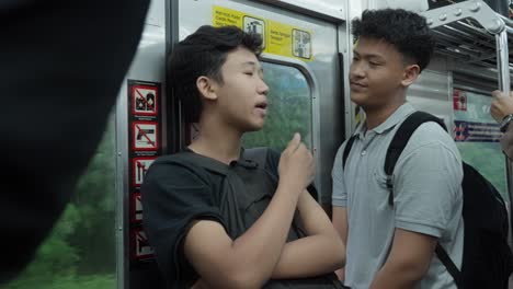 Two-boys-with-backpacks-chat-on-a-busy-commuter-train-in-Tangerang-Selatan