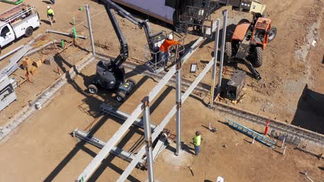 High-angle-aerial-panning-shot-of-construction-crew-working-in-a-bucket-lift-at-a-modular-development-site-in-West-Los-Angeles,-California