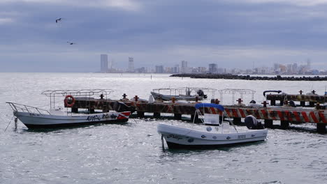 Barcos-Turísticos-Se-Balancean-Sobre-Las-Olas-Del-Océano-Junto-A-Un-Muelle-Comercial-Oxidado,-Cancún.