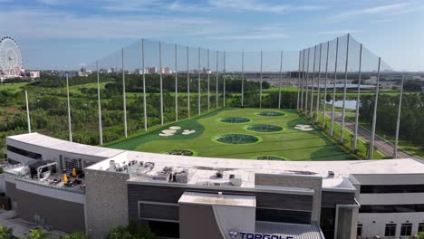 Aerial-view-of-a-TopGolf-entertainment-venue-with-its-large-driving-range,-surrounded-by-lush-greenery