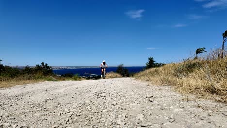 A-person-on-a-bicycle-rides-down-a-dirt-road-in-Crimea,-Russia-on-a-sunny-day