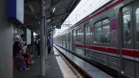 Tren-Rojo-Y-Gris-En-La-Estación-De-Sudimara-En-Un-Día-Nublado-Con-Gente-Esperando-En-El-Andén