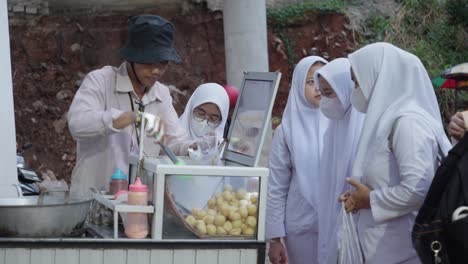 A-street-food-vendor-serves-a-group-of-women-wearing-hijabs-at-Rawa-Buntu-Train-Station