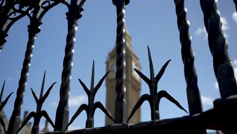 View-Of-blurred-Big-Ben-behind-beautifully-twisted,-sharp-ornate-iron-fence-bars-against-a-clear-blue-sky,-symbolizing-separation-and-grandeur-amidst-modern-urban-civilization