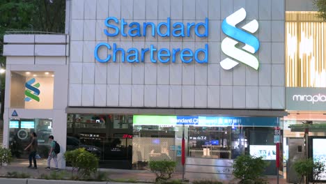 Pedestrians-walk-past-the-British-multinational-banking-and-financial-services-company,-Standard-Chartered,-branch-in-Hong-Kong