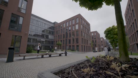 Panning-shot-of-people-walking-through-a-modern-urban-park-surrounded-by-brick-buildings