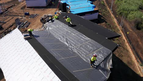 Rising-aerial-shot-tilting-down-at-construction-workers-on-the-roof-of-a-pre-fab-housing-unit-at-a-modular-development-site-in-West-Los-Angeles,-California