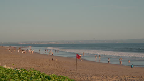 überfüllter-Strand-Von-Seminyak-Im-Sommer-Mit-Gruppen-Von-Menschen,-Die-Am-Meer-Entlang-Spazieren,-Bali,-Indonesien---Weitwinkel-Zeitlupe