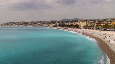 People-Relax-On-Beach-By-Promenade-des-Anglais-In-Nice,-France,-Wide-Aerial-Shot