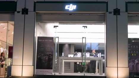 During-a-Hong-Kong-night,-customers-explore-DJI's-official-store,-known-for-its-drones,-while-pedestrians-pass