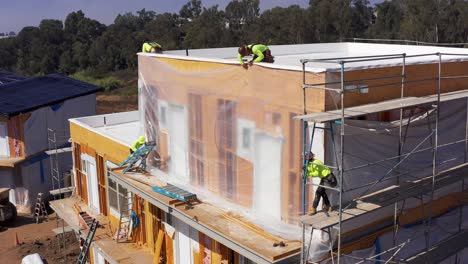 Aerial-close-up-panning-shot-of-construction-workers-siding-a-pre-fabricated-housing-module-at-a-development-site-in-West-Los-Angeles,-California