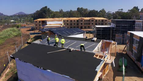 Toma-Aérea-Lenta-De-Un-Equipo-De-Construcción-Trabajando-En-El-Techo-De-Un-Módulo-De-Vivienda-En-Un-Sitio-De-Construcción-Prefabricado-En-El-Oeste-De-Los-Ángeles,-California.