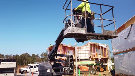 Gimbal-tilting-up-shot-of-a-construction-worker-raising-himself-in-a-lift-crane-at-a-building-site-in-West-Los-Angeles,-California