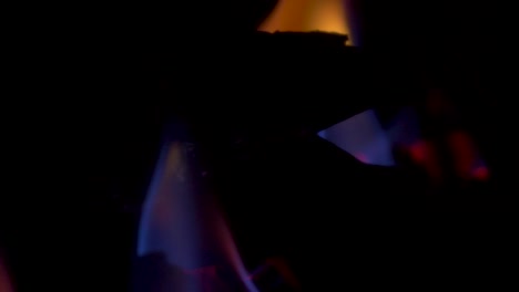 Slow-motion-pan-close-up-of-gas-flame-glowing-embers-hot-on-artificial-wooden-log-fireplace-indoors-household-appliance-energy-electricity-heating