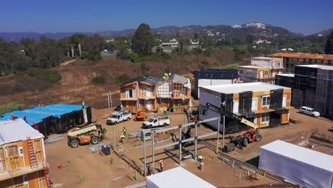 Wide-descending-aerial-shot-of-construction-crew-working-with-a-industrial-lift-crane-at-a-modular-building-site-in-West-Los-Angeles,-California