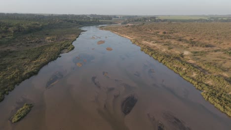 Absteigende-Filmische-Drohnenansicht-Des-Saisonalen-Oder-Kurzlebigen-Crocodile-River-Durch-Ackerland-In-Südafrika