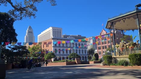 Los-Ángeles-Plaza-Park-En-Un-Día-Caluroso-Y-Soleado,-Pico-House,-El-Ayuntamiento-Y-Banderas-Coloridas,-California,-EE.UU.