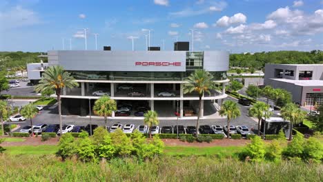 Aerial-view-of-a-modern-Porsche-dealership-showcasing-a-sleek,-multi-level-building-with-cars-on-display-and-palm-trees-surrounding-the-parking-area