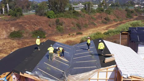 Wide-aerial-panning-shot-of-construction-crew-working-on-the-roof-of-a-pre-fab-housing-unit-at-a-modular-building-site-in-West-Los-Angeles,-California