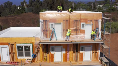 Aerial-rising-and-tilting-down-shot-of-construction-workers-siding-a-pre-fab-module-unit-at-a-building-site-in-West-Los-Angeles,-California