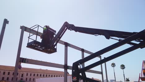 Gimbal-wide-shot-of-a-construction-worker-lowering-in-a-bucket-lift-crane-at-a-modular-development-site-in-West-Los-Angeles,-California