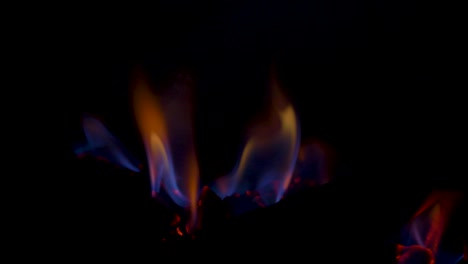 Slow-motion-close-up-shot-of-gas-fireplace-hot-flames-burning-embers-on-charcoal-coal-fake-wooden-logs-behind-glass-panel-household-heating-energy