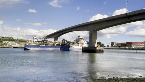 Cargo-ship-passing-under-a-bridge,-viewed-from-the-Summer-Feastival-by-Street-Food-Circus,-with-cityscape-in-the-background