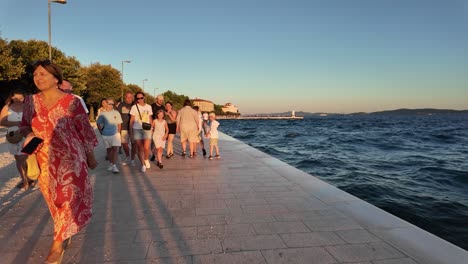 Walking-opposite-of-crowds-of-people-going-to-watch-the-sunset-in-Zadar,-Croatia-on-the-seafront-promenade